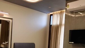 A hotel room with a bed, a chair, a desk with a television, and an air conditioning unit. - Hotel Sky Inn (Sikar)