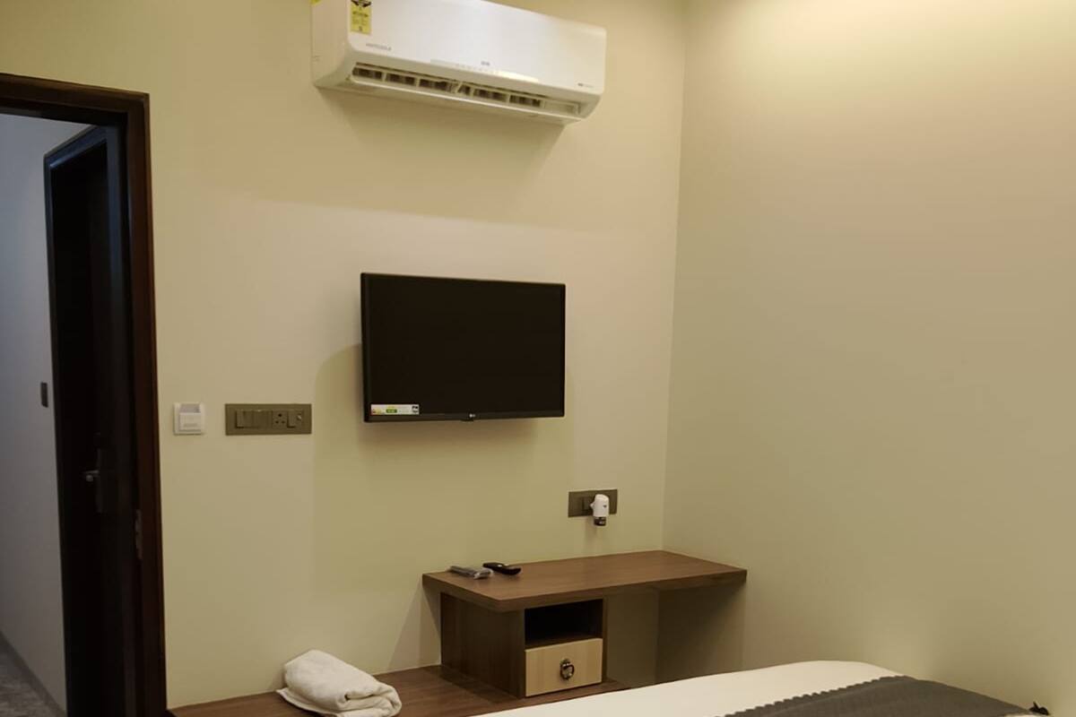 Una camera d'albergo con un letto, una TV fissata al muro, un comodino con un telecomando e un condizionatore d'aria.