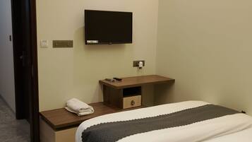 Una habitación de hotel con una cama, un televisor montado en la pared, una mesita de noche con un control remoto y un equipo de aire acondicionado.