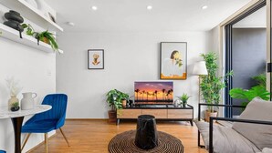 Een moderne woonkamer met een houten vloer, een blauwe stoel, een zwarte salontafel en een schilderij van een zonsondergang.