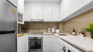 Een kleine keuken met witte kasten, een roestvrijstalen koelkast, een magnetron, een vaatwasser, een oven en een wasmachine.