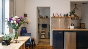 A modern kitchen with a wooden countertop, a built-in dishwasher, and a small dining area with a table and chairs. - Beachfront Bondi Studio with Aircon (North Bondi)