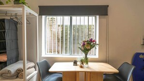 A room with a window, a table with two chairs, a plant, and a shelf with folded towels. - Beachfront Bondi Studio with Aircon (North Bondi)