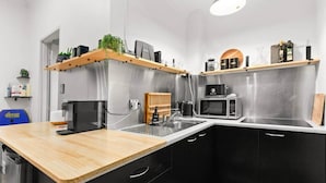 A modern kitchen with black cabinets, a wooden countertop, a coffee machine, a microwave, and a hanging plant. - Beachfront Bondi Studio with Aircon (North Bondi)