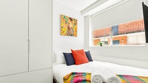 Un dormitori modern amb un llit gran, llençol de colors i una finestra amb vista a un edifici de maó.