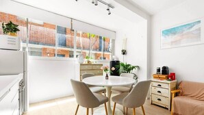 Una cuina moderna amb zona de menjador, un gran finestral amb vista a un edifici de maó i una zona d'estar acollidora amb una manta.