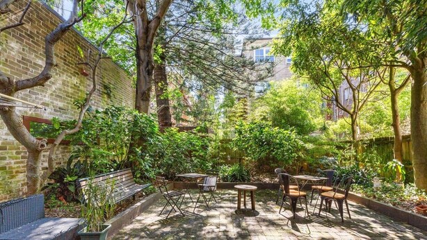 Un patio con muros de ladrillo, un banco de madera y mesas.