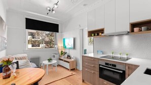 Een moderne keuken met een ingebouwde kookplaat, houten kastjes en een groot raam met uitzicht op bomen.