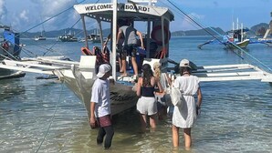 A boat with a 'WELCOME ABOARD!' sign, passengers boarding, and a clear view of the water and other boats in the background. - Apoheo Beach Cabin (El Nido)