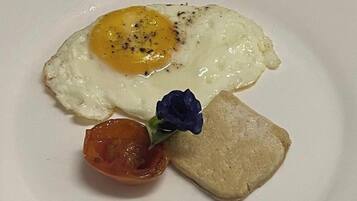 Un plato con un huevo frito, una rodaja de tomate y una tostada.