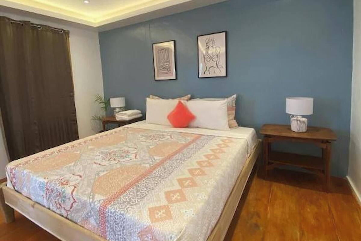 Un dormitorio con una cama, una mesita de noche, una lámpara y dos cuadros en la pared.