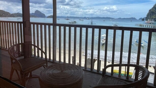 A balcony with a view of the sea, wooden chairs, and a woven table. - Apoheo Beach Cabin (El Nido)