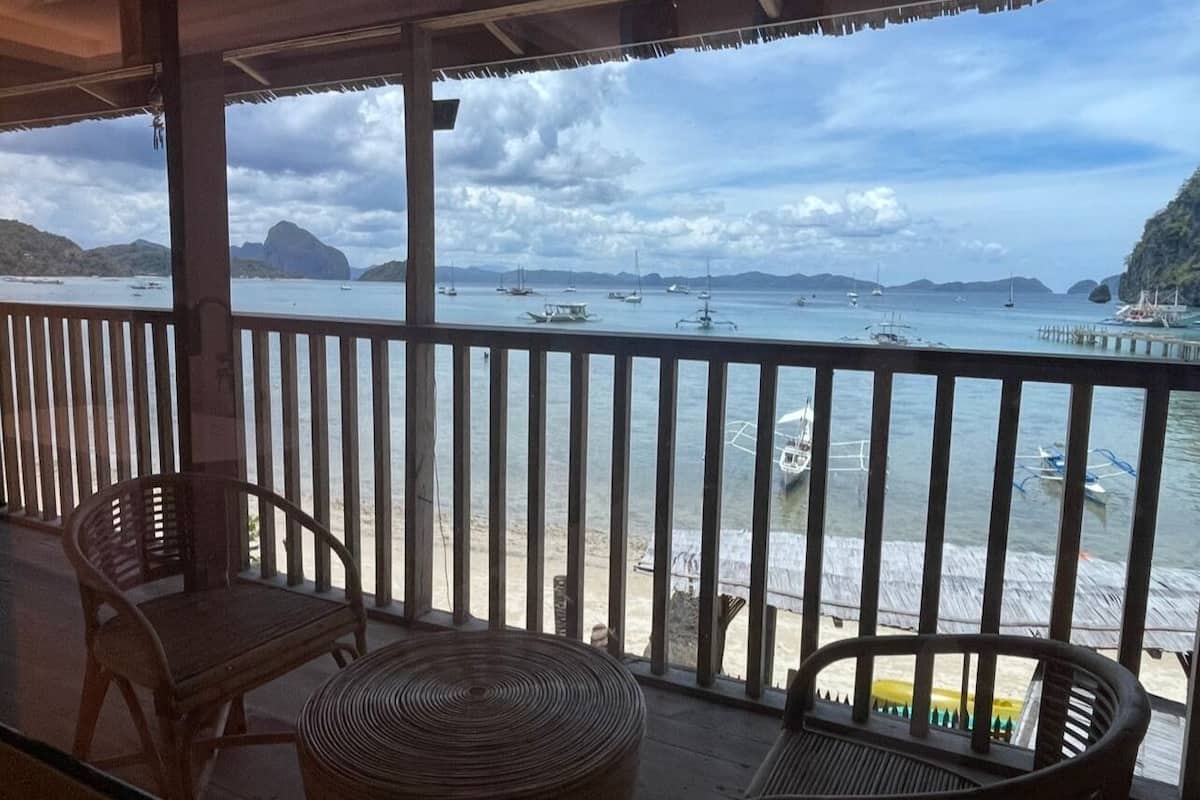 Un balcón con vista al mar, sillas de madera y una mesa de fibras naturales.