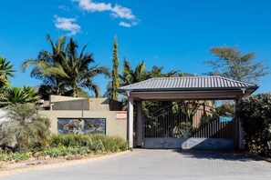 A gated entrance with a metal gate and a covered walkway, surrounded by palm trees and greenery. - Marangie 2-Bedroom Apartment | Peaceful Family Retreat & Business-Ready Stay (Lusaka)