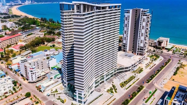 A high-rise hotel with a curved facade, located near a beach and a coastal road. - Apartment FLC Quy Nhơn Sea View (Quy Nhon Nam)