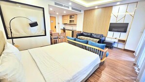 A hotel room with a large bed, a seating area with a sofa and chairs, a small kitchen, and a TV mounted on the wall. - Apartment FLC Quy Nhơn Sea View (Quy Nhon Nam)