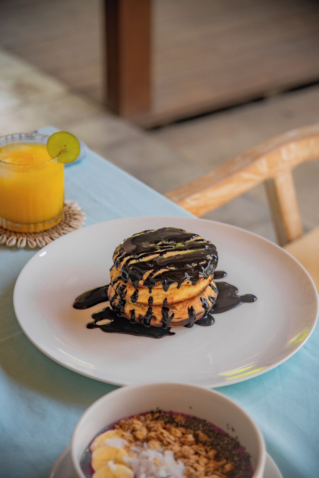Un dessert présenté dans une assiette, nappé de chocolat fondu, un verre de jus d’orange et un bol de céréales avec du lait.
