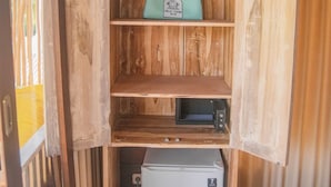 A wooden cabinet with a teal bag on the top shelf, a microwave, and a small refrigerator. - Villa Tahid (Gili Air)