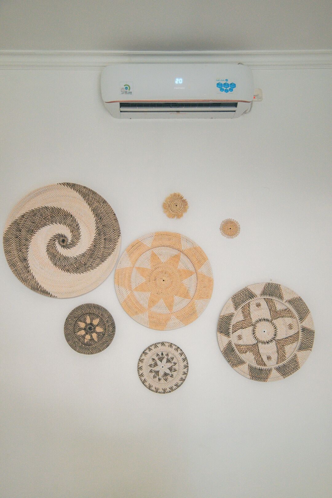 A wall with five circular woven wall hangings of varying patterns and sizes.
