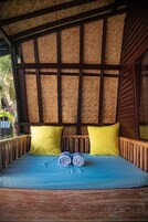 A bed with a blue mattress and two yellow pillows, a rolled towel, and a woven headboard.