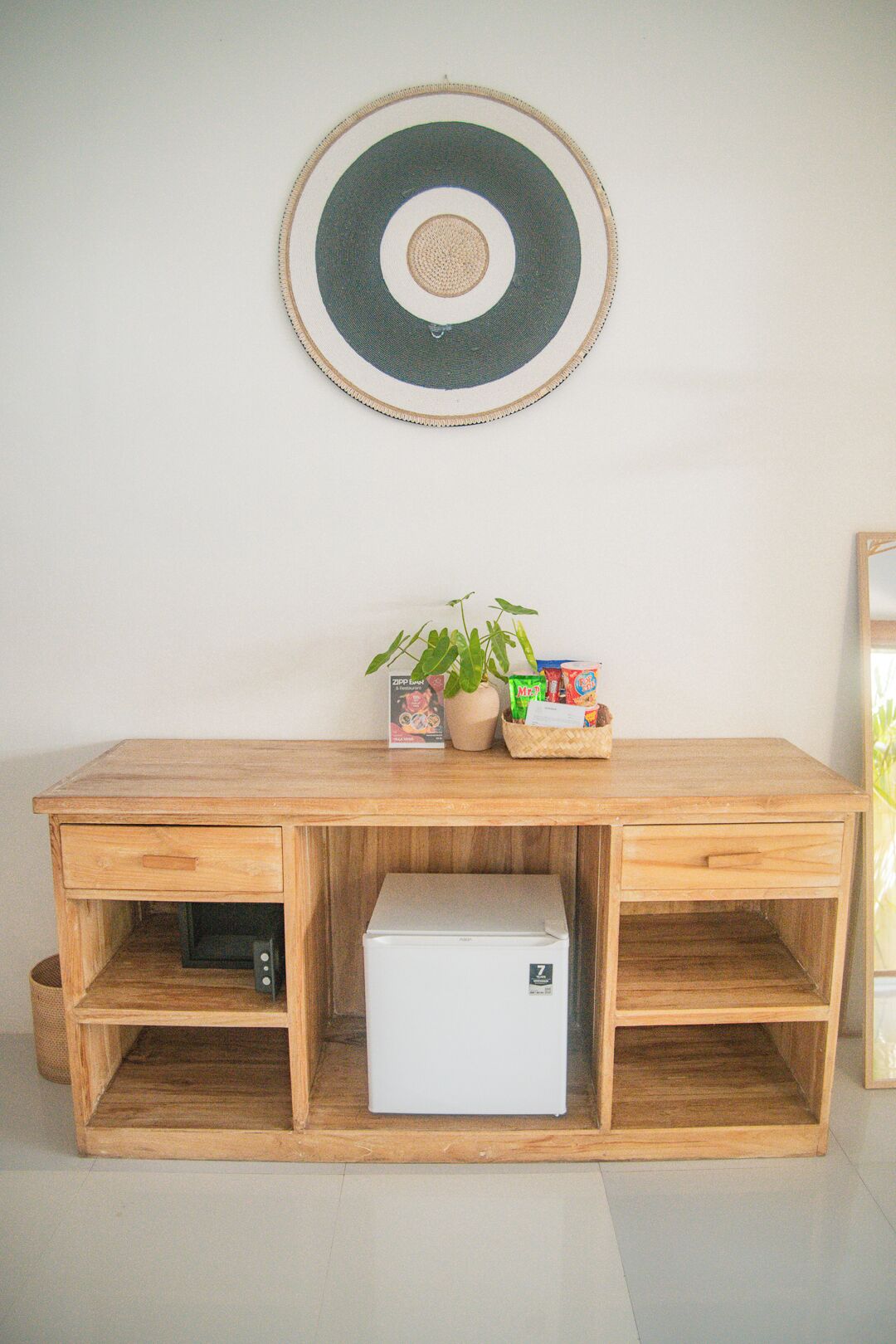 Et træskrivebord med indbygget minibar, en potteplante og en kurv med snacks.