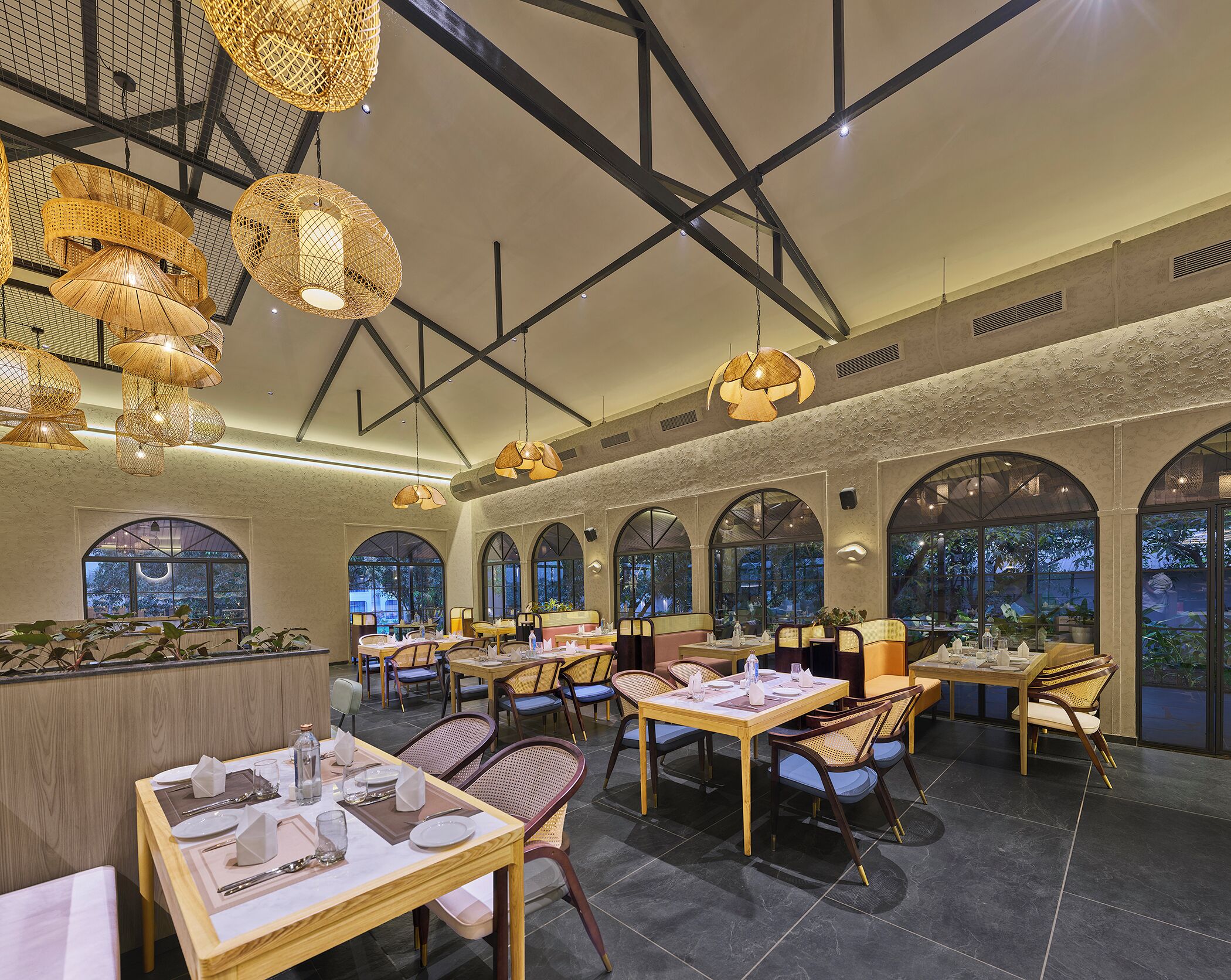 Un restaurant doté de nombreuses tables et chaises, de grandes fenêtres et de lampes en osier suspendues au plafond.