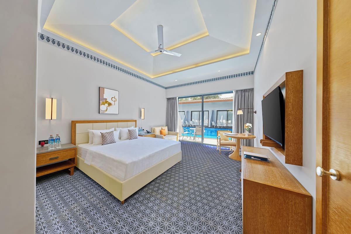 Une chambre d’hôtel avec un grand lit, une télévision, un bureau avec une chaise, une petite table avec un vase et une vue sur la piscine.
