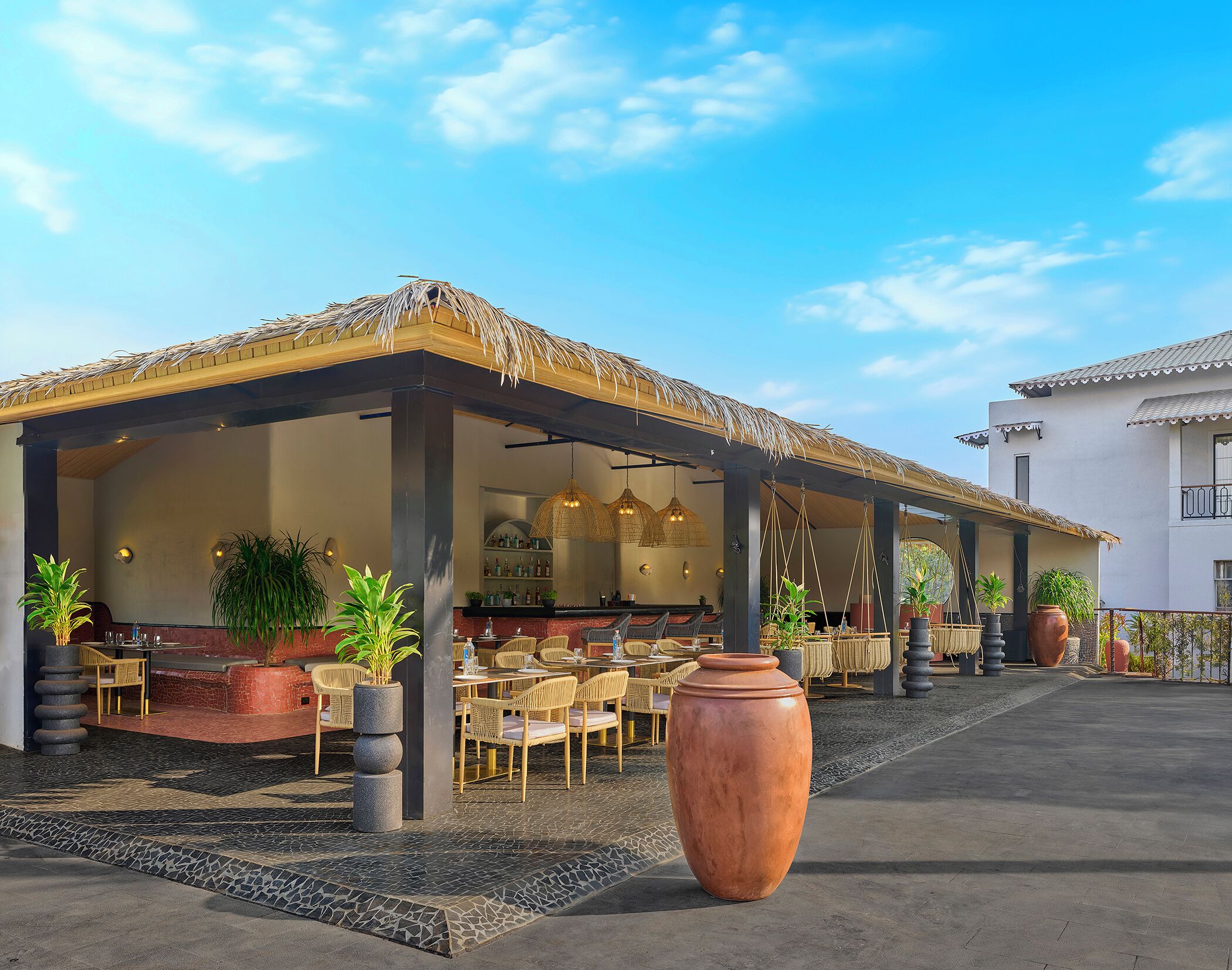 Un área de comedor al aire libre con techo de paja, mobiliario de mimbre y plantas en macetas.
