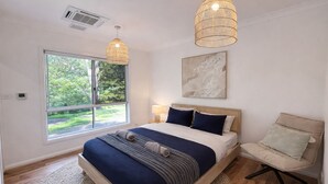 A bedroom with a large bed, a chair, a window, and two pendant lights.