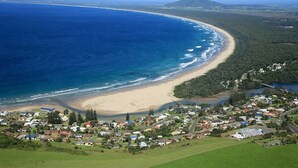 An aerial view of a coastal town with a beach, houses, and greenery.