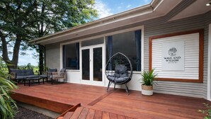 A modern house with a wooden deck, a swing chair, and a sign for 'Wave and Willow Retreat'.
