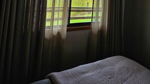 Een slaapkamer met een groot raam, gordijnen en een bed.