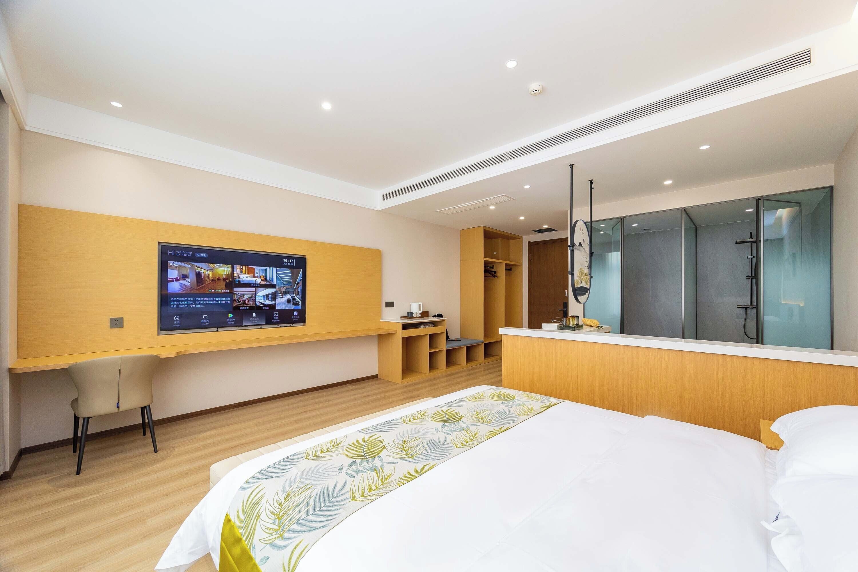 A modern hotel room with a large bed, a TV mounted on the wall, a desk, and a walk-in closet.