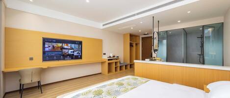 A modern hotel room with a large bed, a TV mounted on the wall, a desk, and a walk-in closet.