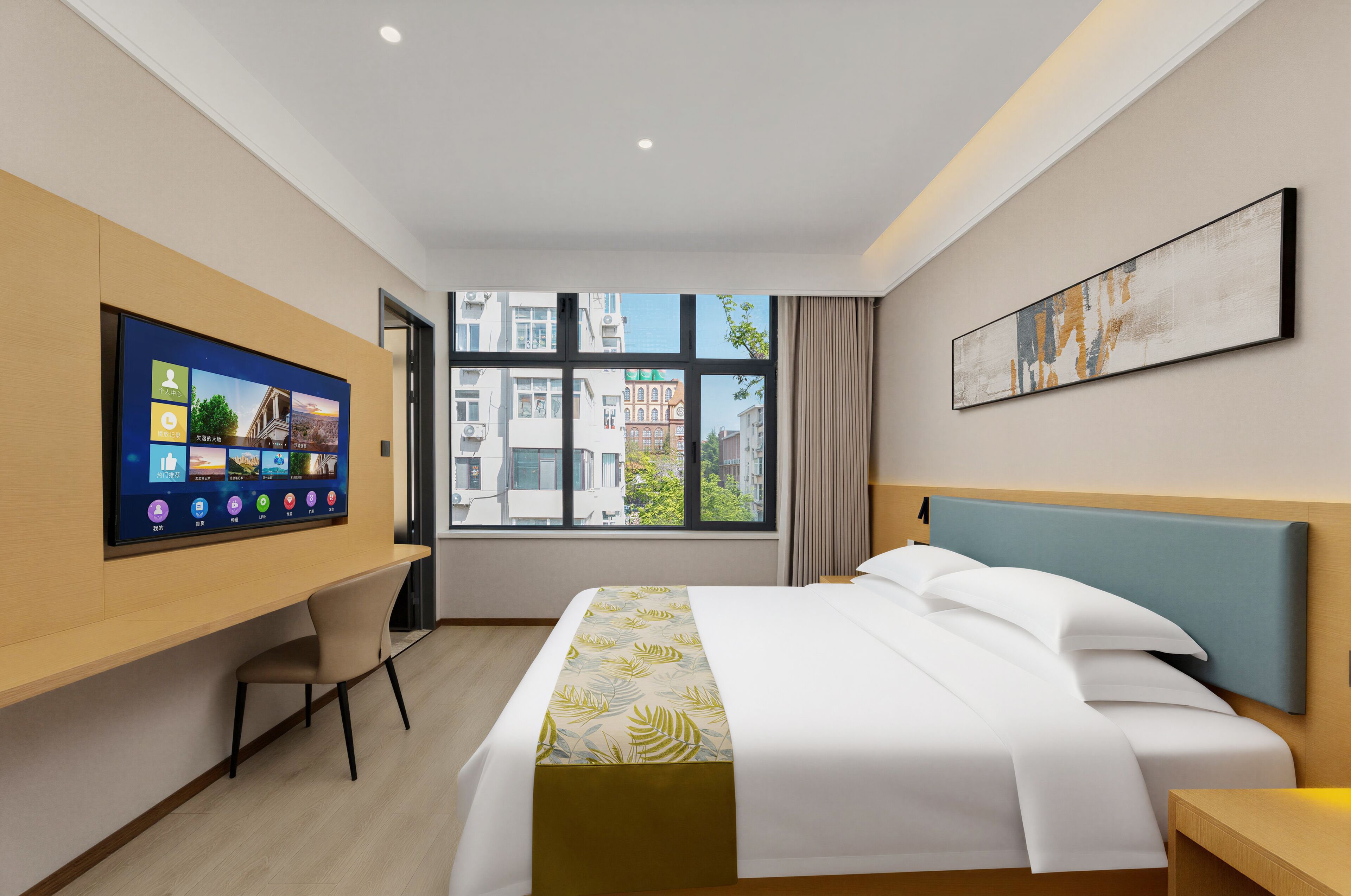 Ein Hotelzimmer mit Bett, Schreibtisch, Fernseher und Fenster mit Blick auf die Stadt.