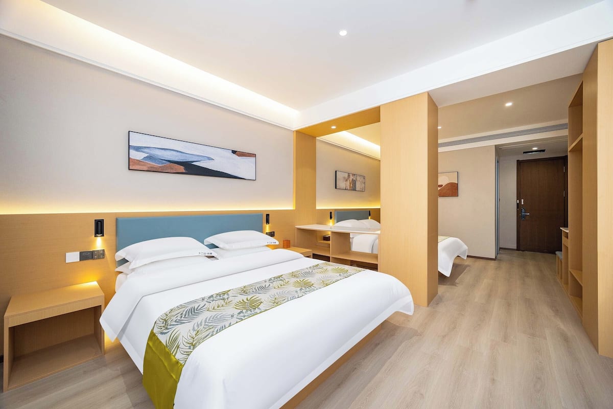 Une chambre d’hôtel moderne avec un grand lit, des tables de chevet, une petite table, un miroir et une porte donnant sur une salle de bain.