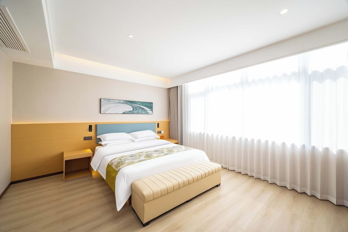 Une chambre d’hôtel moderne avec un lit, un banc et une grande fenêtre avec des rideaux.