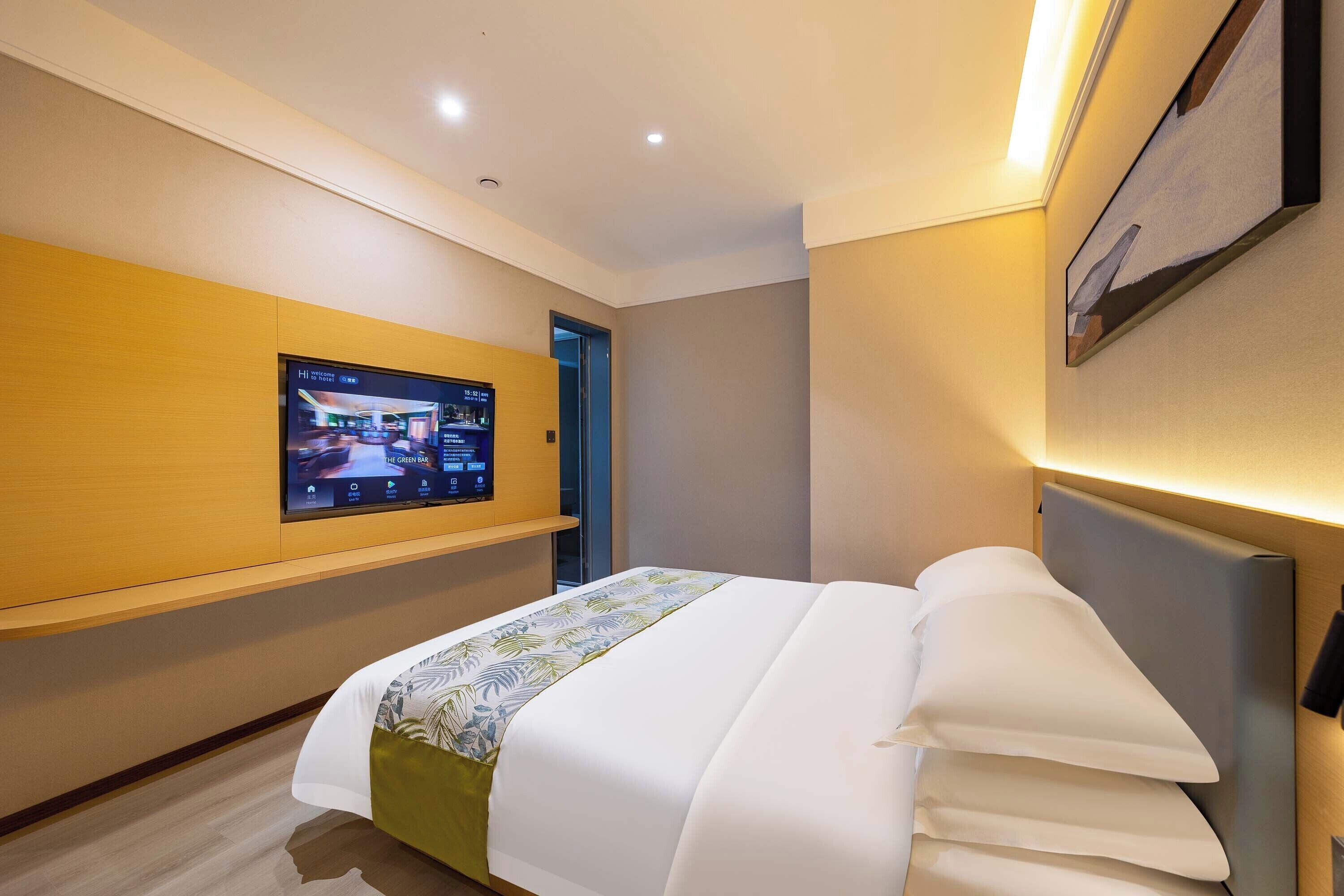 A modern hotel room with a large bed, a mounted TV, and a wooden panel wall.