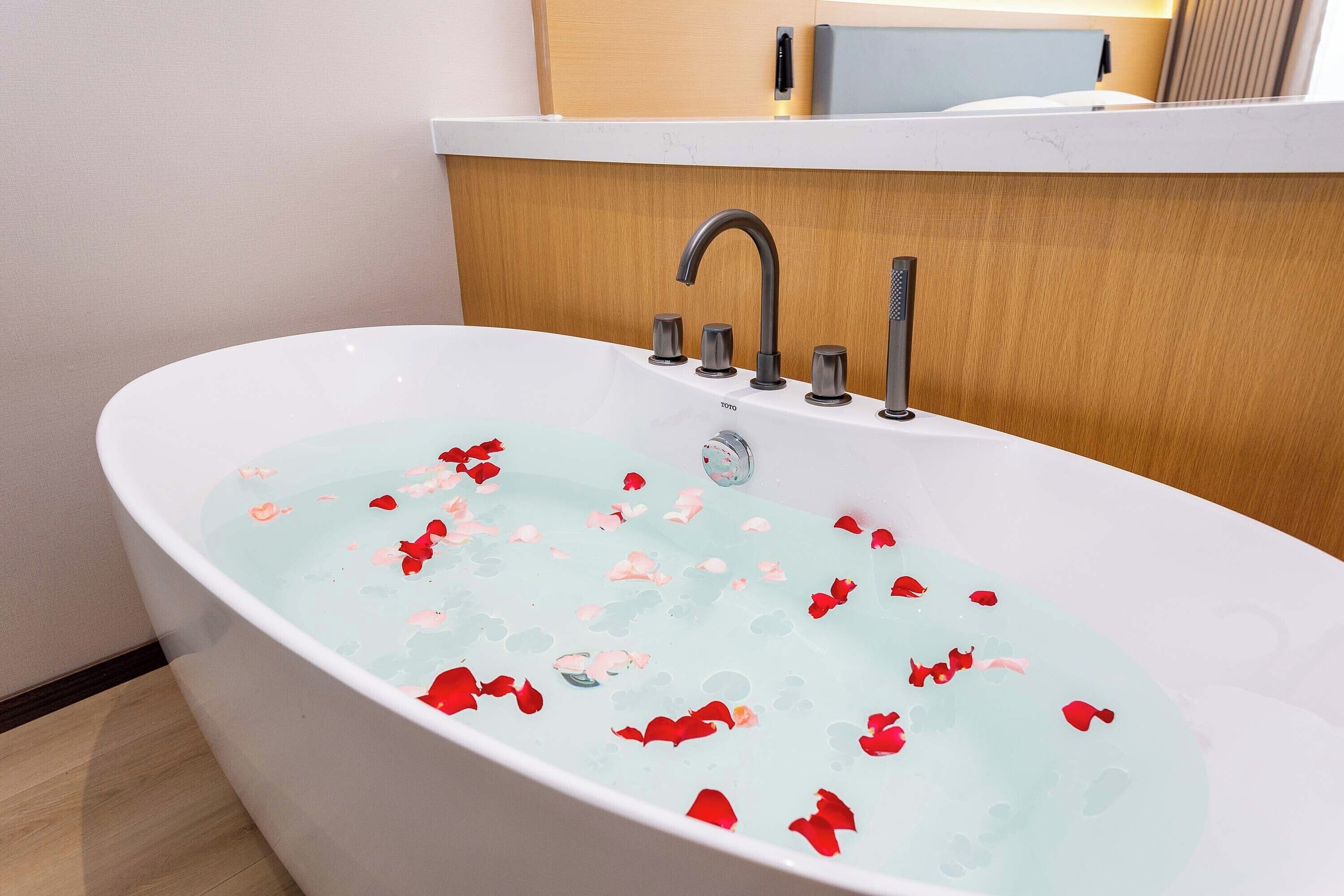 Un baño moderno con una bañera independiente llena de agua y pétalos de rosa.