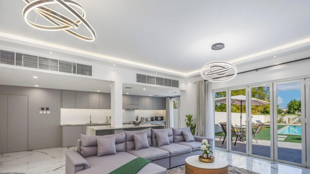 A modern living room with a grey sofa, a coffee table, and a view of a pool and garden through large sliding doors. - LUX The Serene Springs Villa 2 (Dubai)
