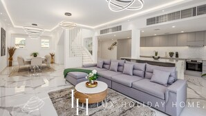 A modern living room with a grey sofa, a coffee table, and a staircase leading to an upper floor. - LUX The Serene Springs Villa 2 (Dubai)