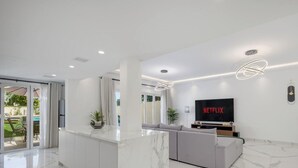 A modern living room with a marble floor, a grey sofa, a TV displaying 'NETFLIX', and a ceiling with recessed lighting and pendant lights. - LUX The Serene Springs Villa 2 (Dubai)
