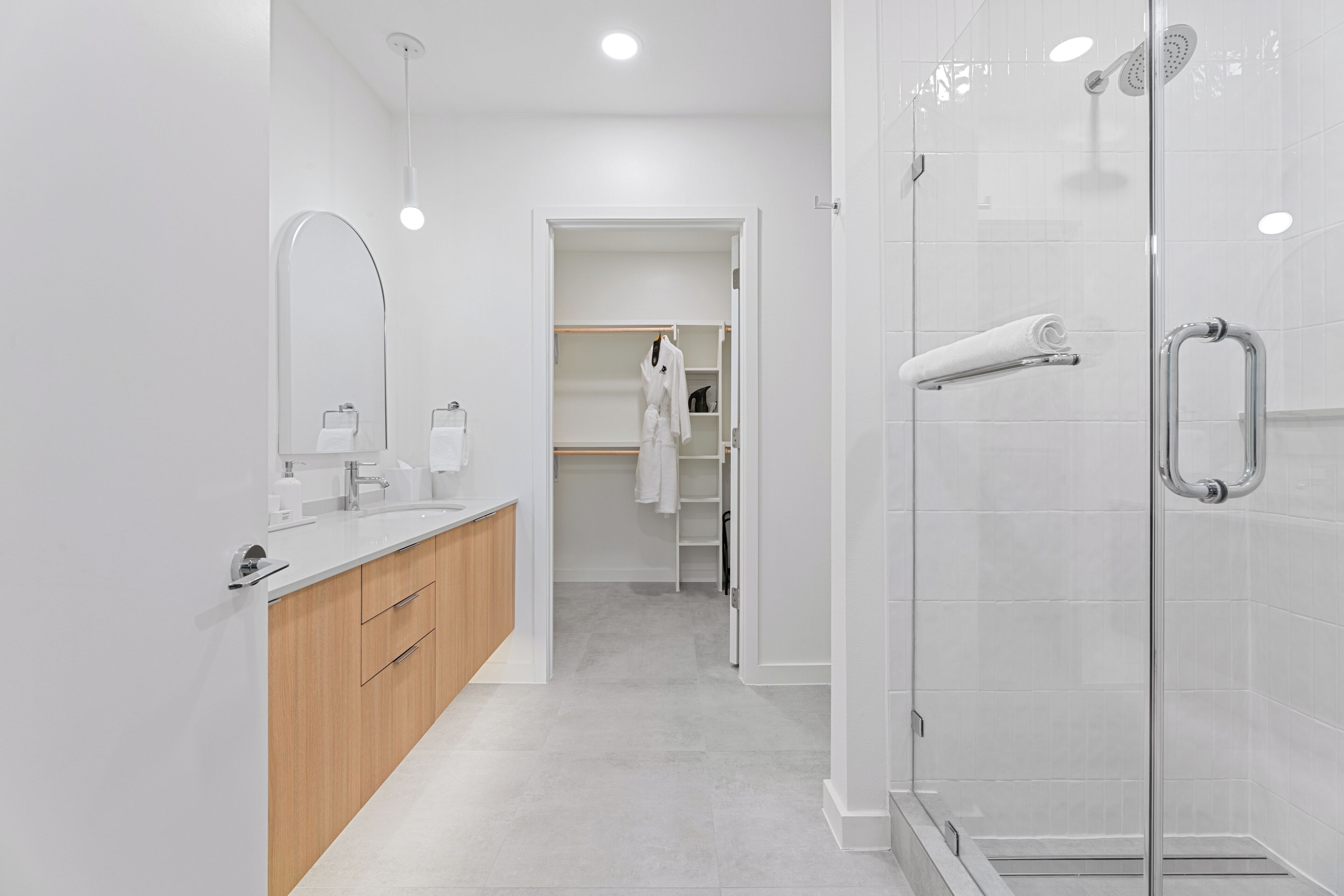 Een moderne badkamer met een douchecabine van glas, een houten wastafelmeubel en een inloopkast.