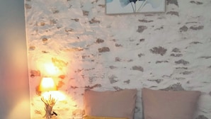 Une chambre à coucher avec un lit, une table de chevet, une lampe et un mur orné d’un tableau représentant des motifs floraux.