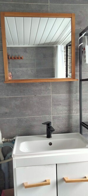 Une salle de bain avec un lavabo blanc, des poignées en bois, un robinet noir et un miroir avec un cadre en bois.
