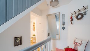 A staircase with a white railing, a mirror, a wall-mounted wreath, and a cushion with a floral design. - Black Forest Apartment "Onkel Franz" for 4 Guests & Baby, Pets Welcome, Near Europa Park (Ohlsbach)