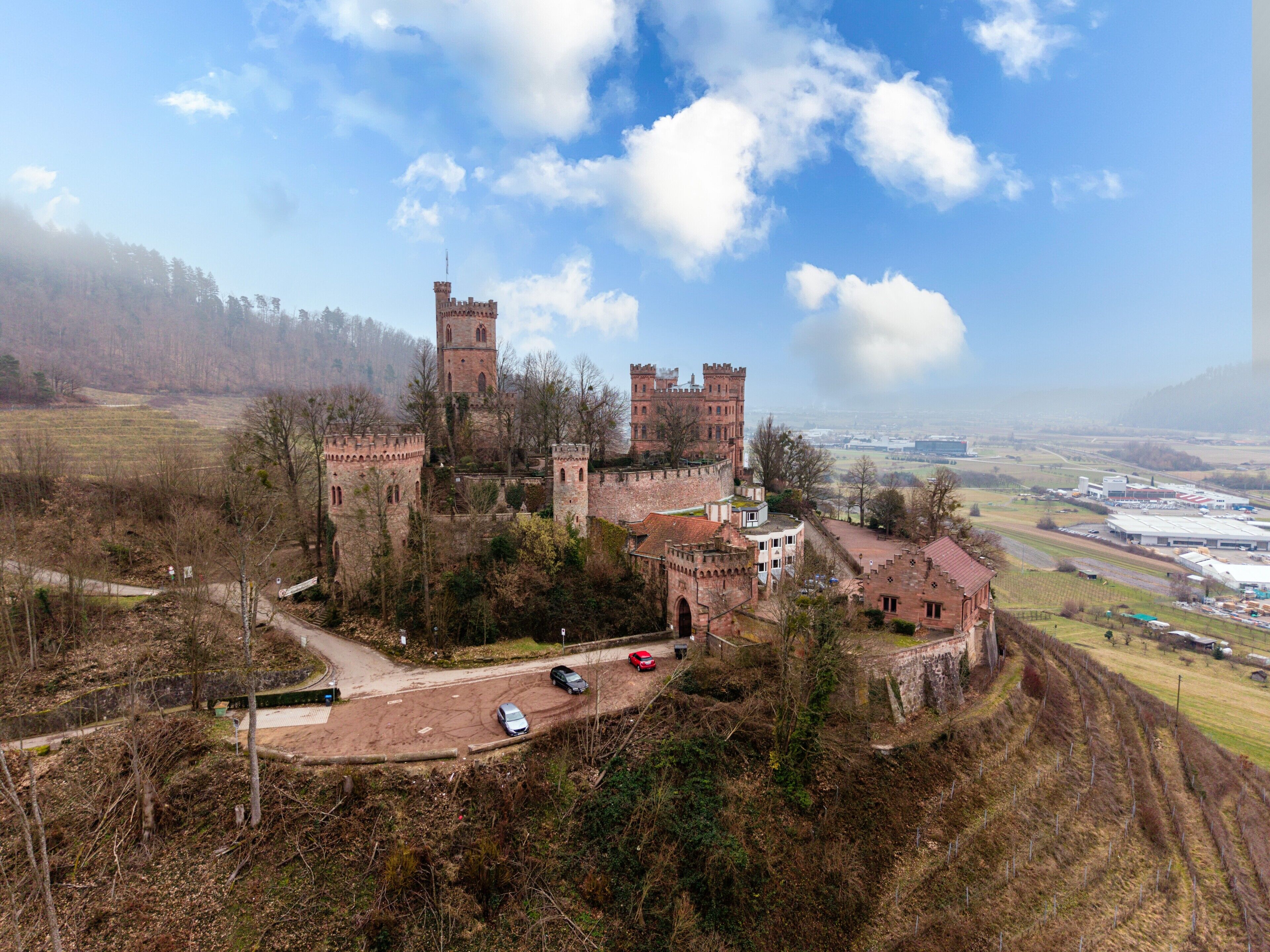 A castle with multiple towers, surrounded by a hilly landscape and a clear sky.