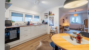 A modern kitchen with white cabinets, a wooden countertop, and a dining area with a table and chairs. - Black Forest Apartment "Onkel Franz" for 4 Guests & Baby, Pets Welcome, Near Europa Park (Ohlsbach)