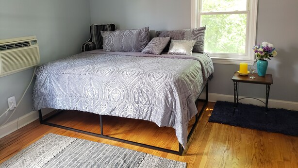 A bedroom with a bed, a window, a bedside table with a vase, and a rug.