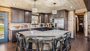 A modern kitchen with dark wood cabinets, a large island with bar stools, stainless steel appliances, and a wooden ceiling. - Mountain View + Loft + Game Room + Hot Tub | Near Gatlinburg | Vixen Run Lodge (Gatlinburg)